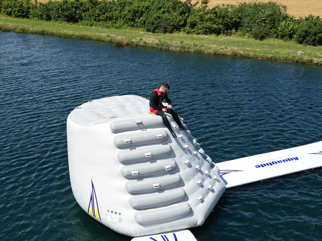 Man sitting on a large inflatable structure on a lake, surrounded by greenery.