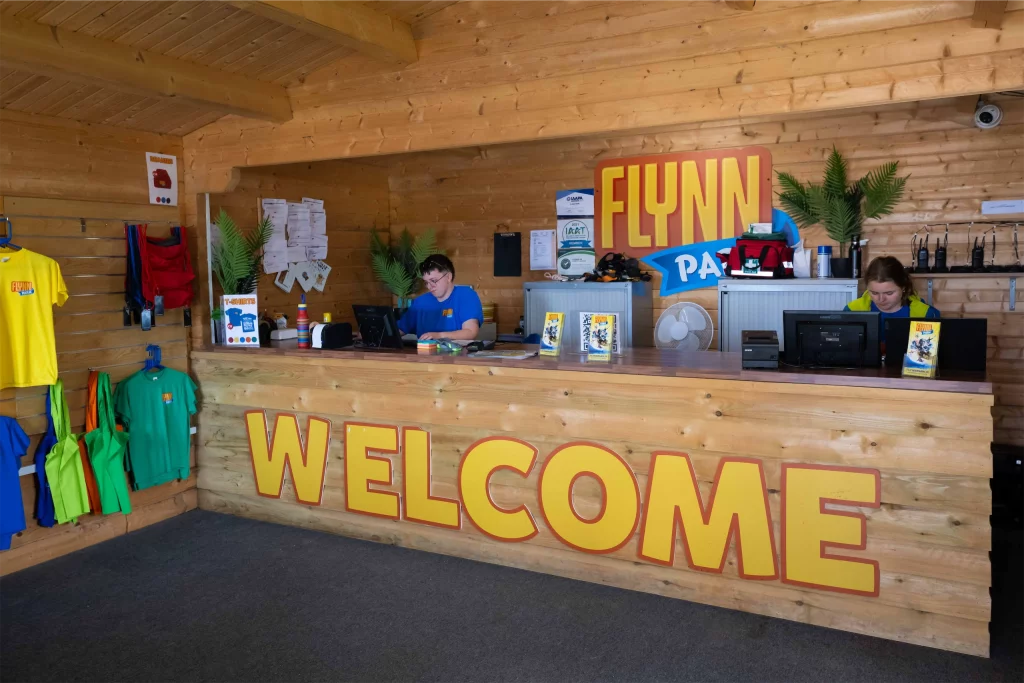 Welcome desk in Flynn Park with staff at computers, colourful t-shirts on display, and a wooden interior.