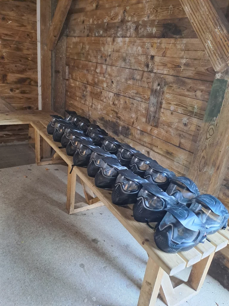 A row of paintball masks on a wooden bench in a rustic cabin.