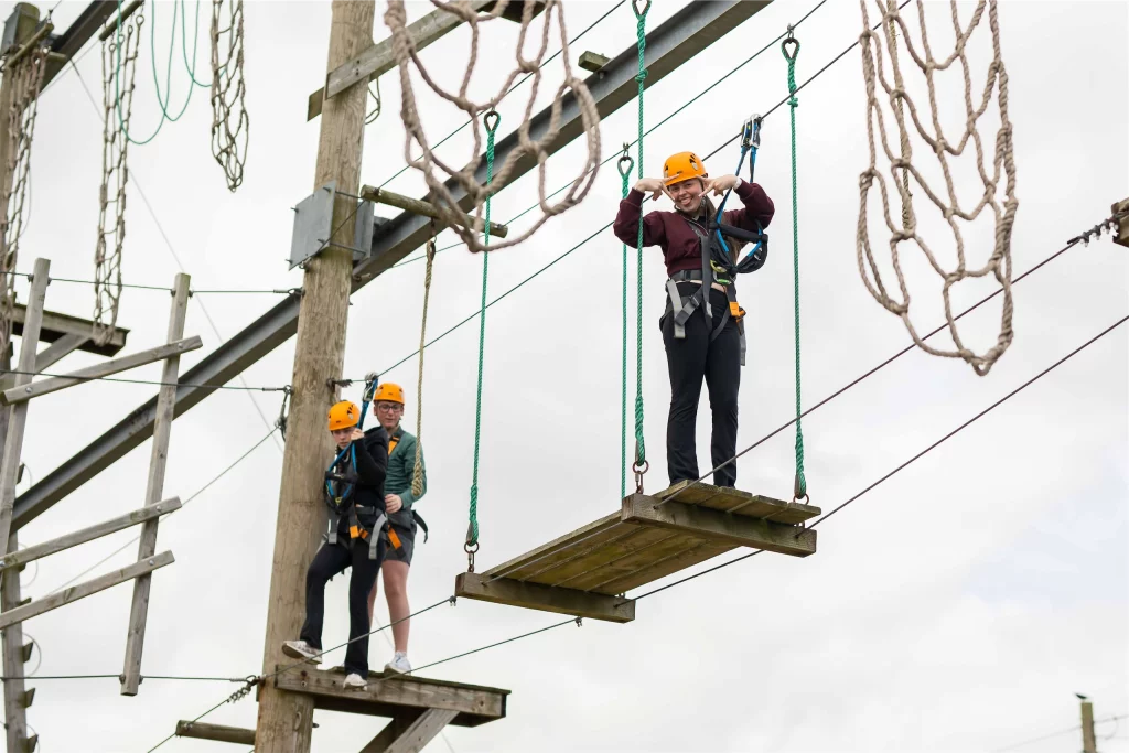 People on a high ropes course wearing helmets and harnesses, balancing and enjoying the adventure activity.