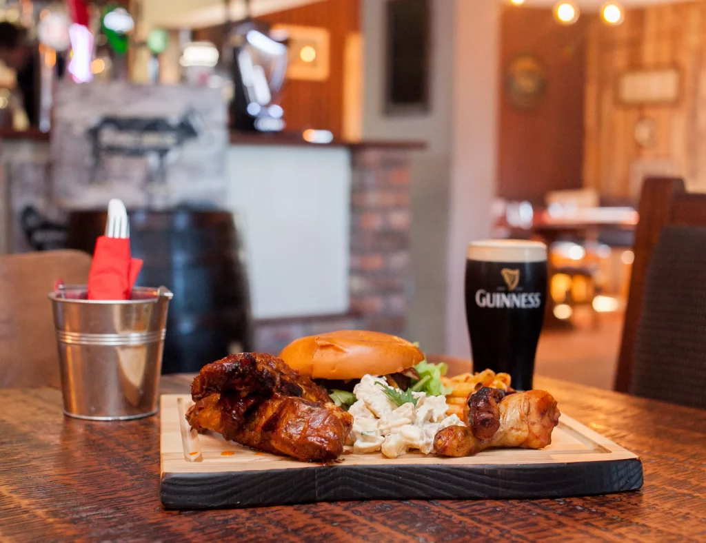 Burger with chips and coleslaw served with a pint of Guinness on a rustic pub table.