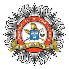 Dublin Fire Brigade emblem with gold helmet, axes, and scales framed by a ribbon. Latin motto encircles the central shield.