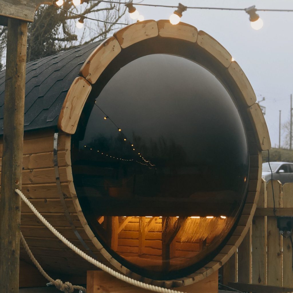 Barrel sauna with warm lights and misty reflection, outdoor setting.