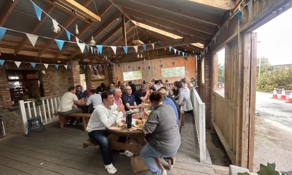People dining in a rustic outdoor café with wooden beams and colourful bunting, enjoying a casual meal.