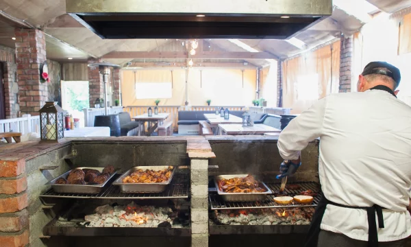 Chef grilling meat and buns on a charcoal grill in a rustic restaurant setting.