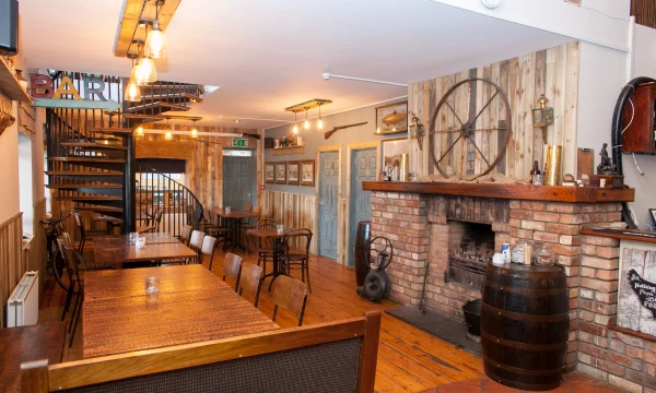 Inviting pub interior with wooden tables, a brick fireplace, spiral staircase, and rustic decor creating a cosy atmosphere.