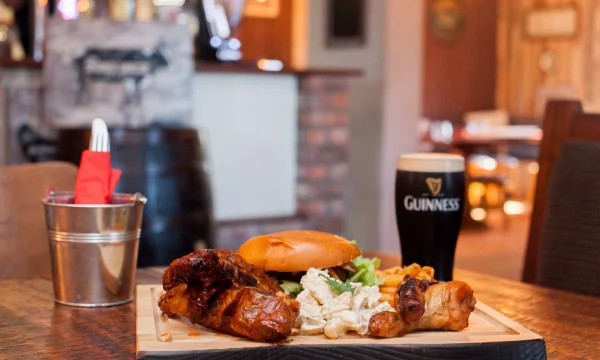 Pub meal with chicken, coleslaw, chips, and a pint of Guinness on a wooden table in a cosy Irish pub setting.