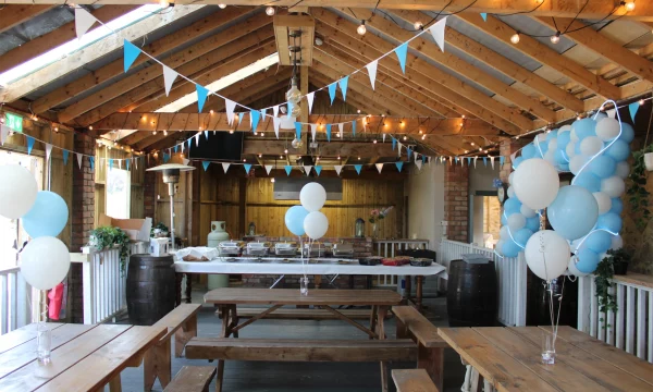 Rustic venue decorated with blue and white balloons, bunting, and string lights, ready for a celebration.